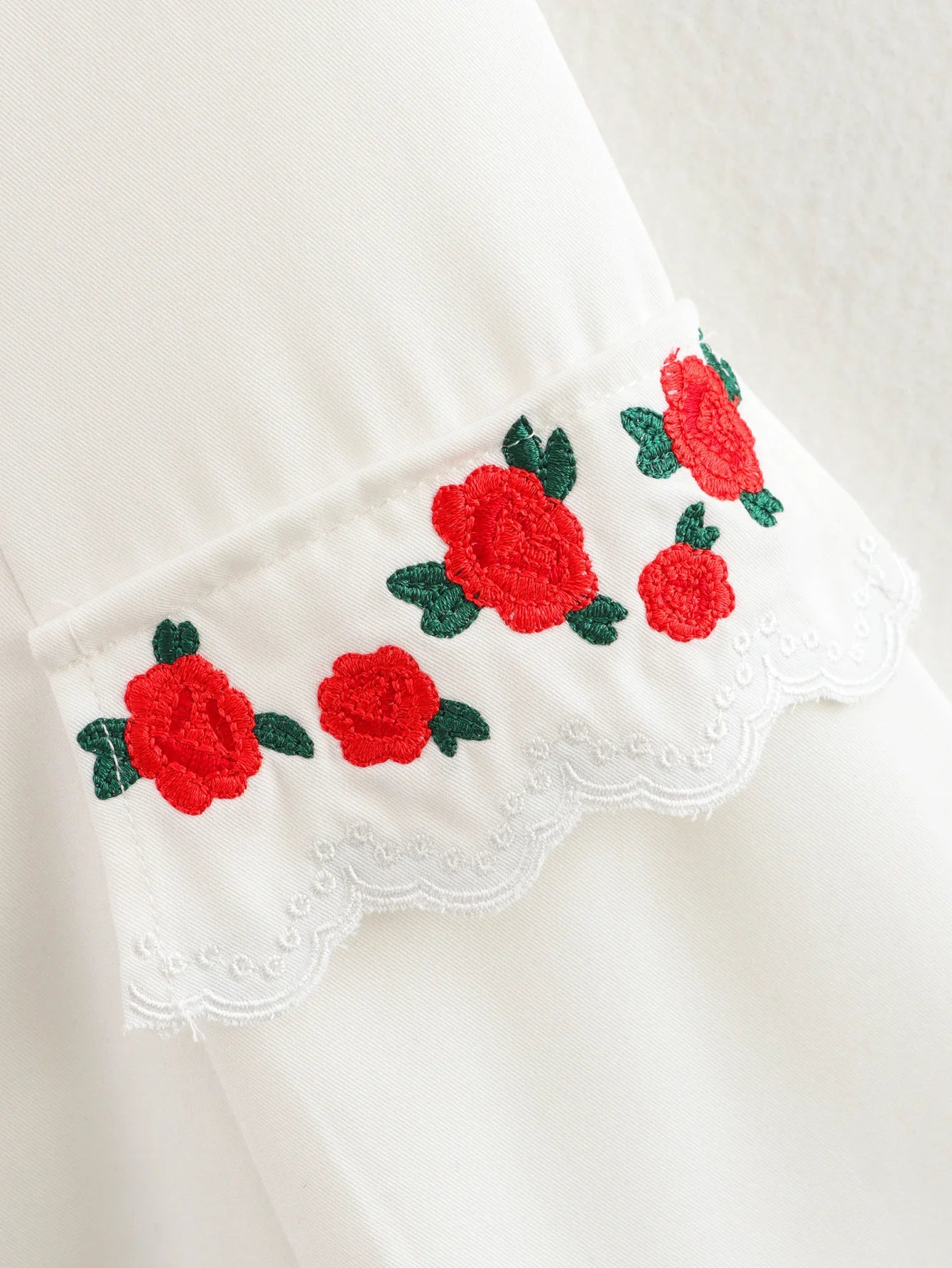 Embroidered red roses with green leaves on a white fabric background