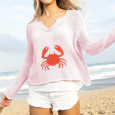Person wearing a pink sweater with a red crab design on a beach.