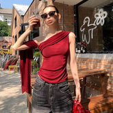 Woman in a red top and sunglasses holding a drink, standing in front of a brick building with a store front.