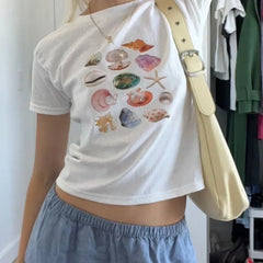 Person wearing a white t-shirt with shell designs and light blue shorts, holding a beige bag.