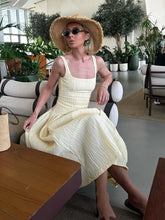 Woman in a yellow dress and straw hat sitting in a modern indoor setting with plants.