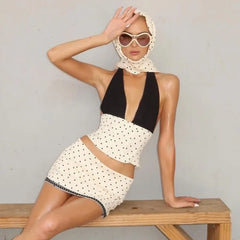 Woman wearing a black and white polka dot dress with sunglasses and headscarf on a gray background