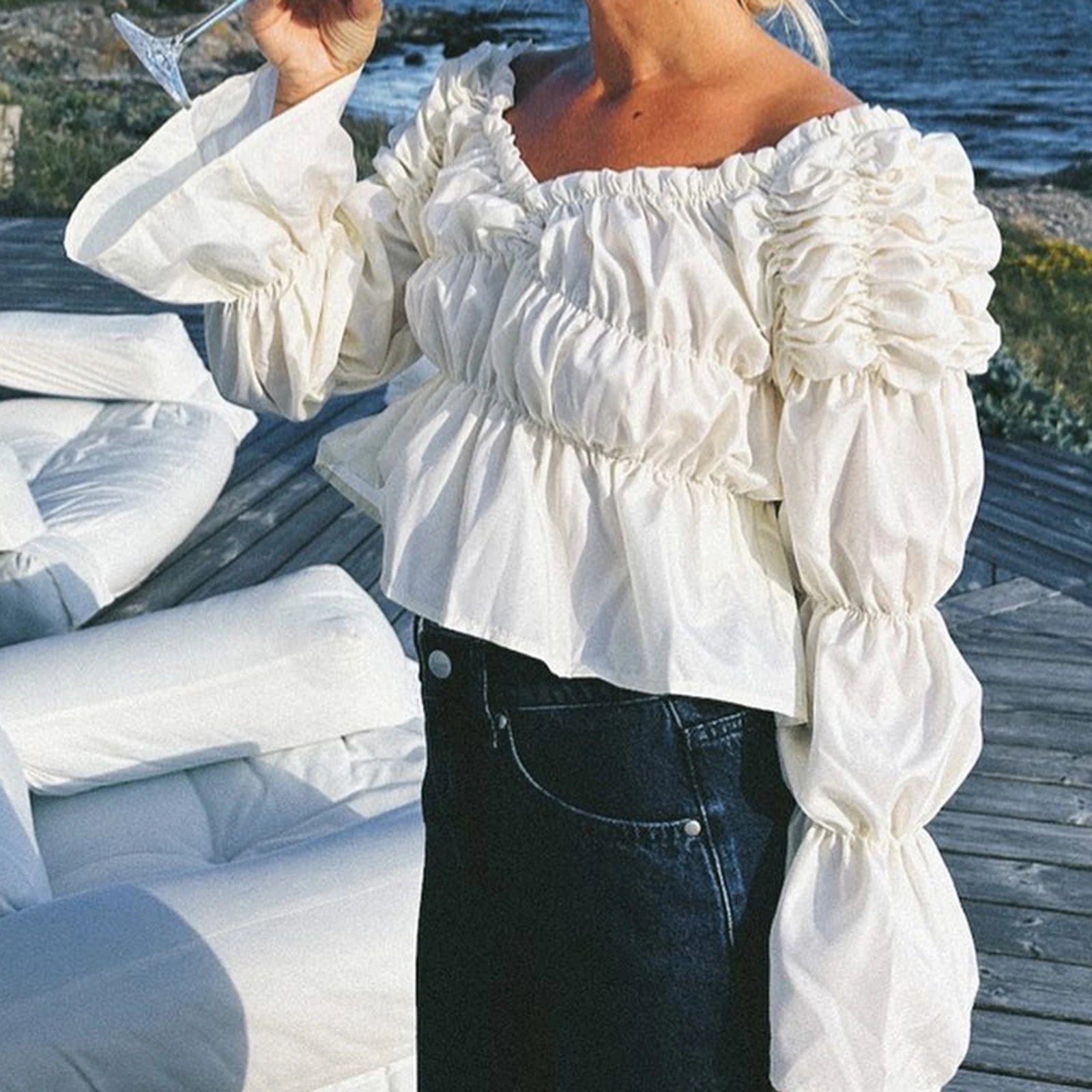 Person wearing a white off-shoulder blouse with puffed sleeves by a waterfront.