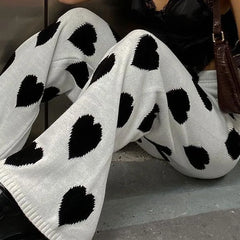 White pants with black heart patterns worn by a person sitting on a bench.