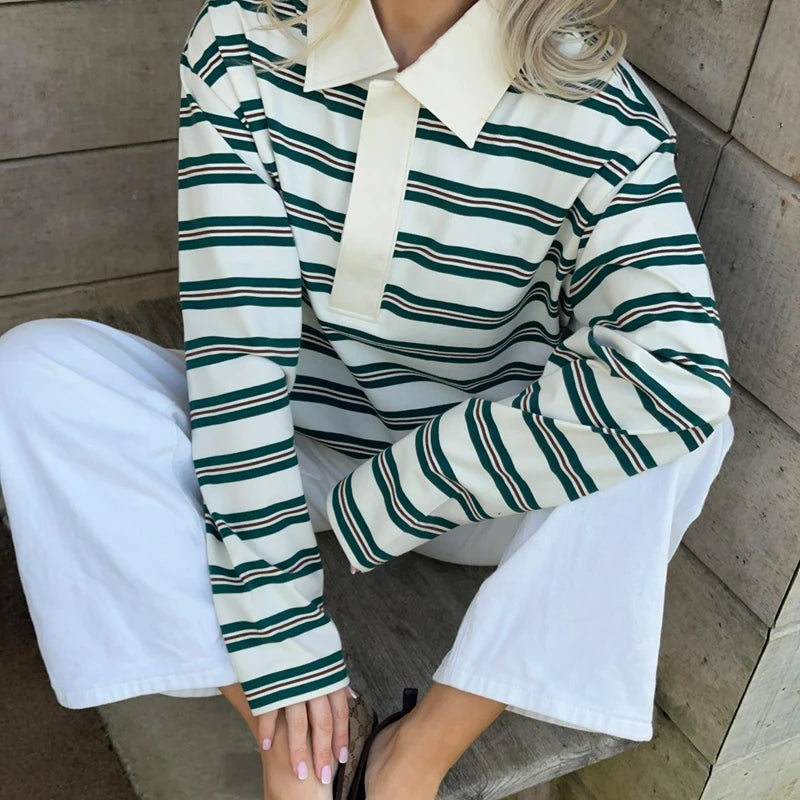 Person wearing a green and white striped shirt with a high collar, sitting on a concrete surface.