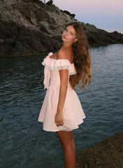 Woman in a pink dress standing by a body of water with a scenic background