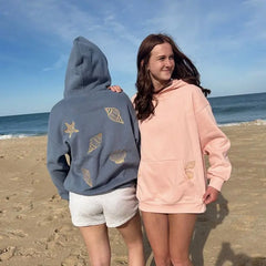 Two people wearing hoodies on a beach with ocean in the background