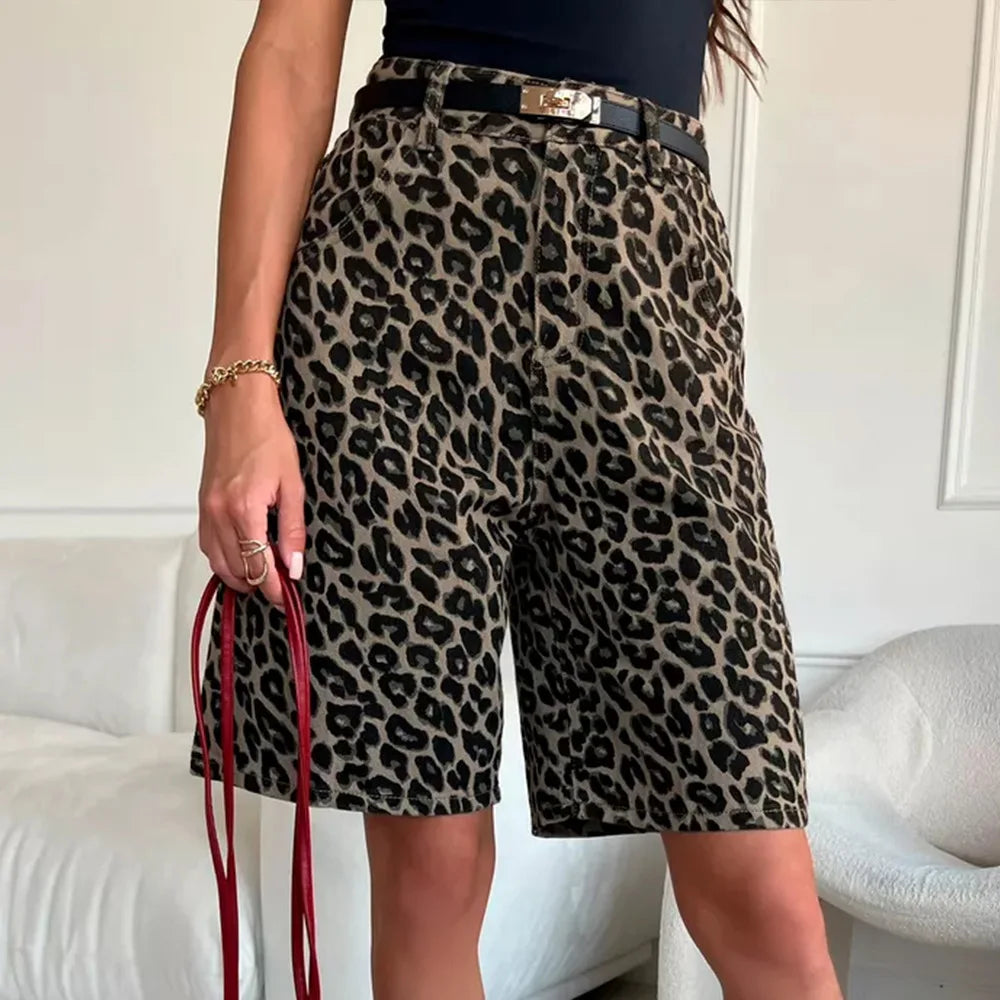 Person wearing leopard print shorts holding a red bag indoors.