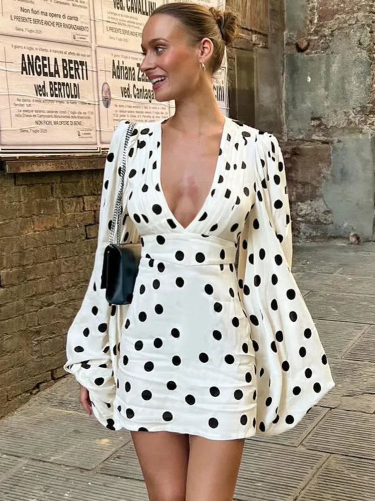 Woman wearing a white polka dot dress with long sleeves in an urban setting.