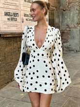 Woman wearing a white polka dot dress with long sleeves in an urban setting.