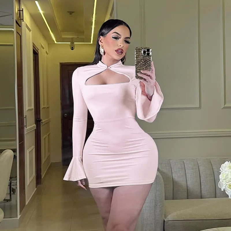 Woman in a light pink dress taking a mirror selfie in an indoor setting.