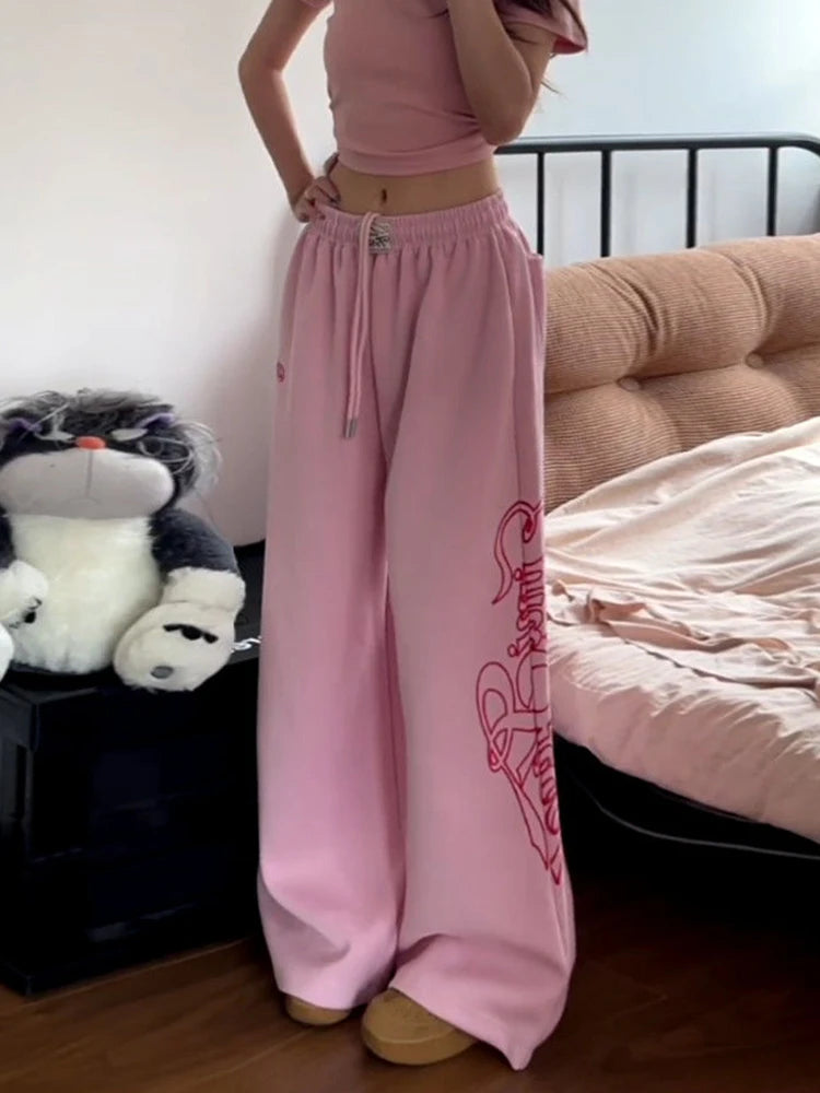 Person wearing pink sweatpants with a logo in a bedroom setting