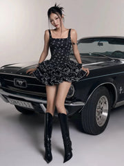 Woman in a black dress and knee-high boots posing in front of a classic car.