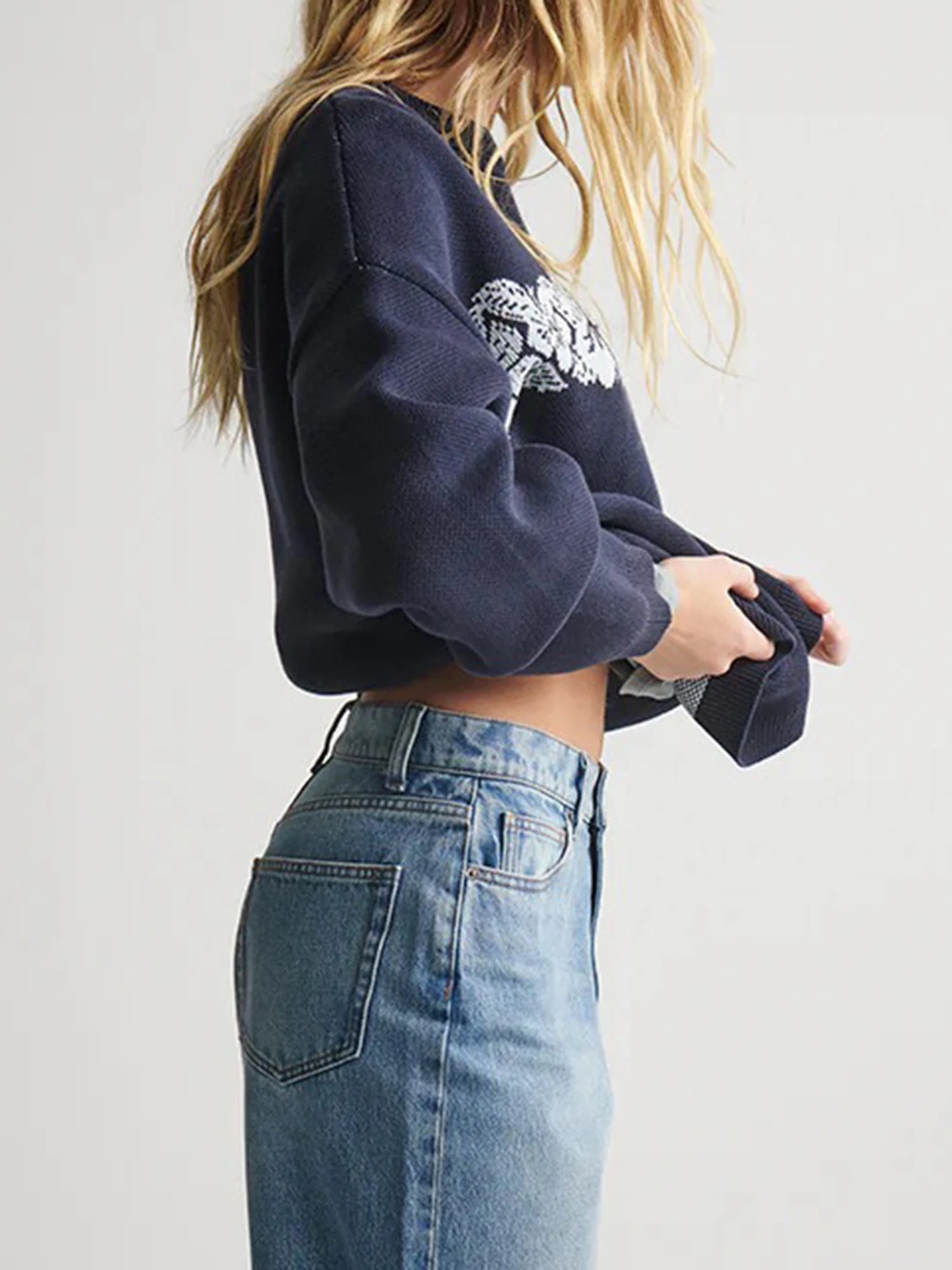 Person wearing a navy blue sweatshirt with a graphic design and blue jeans