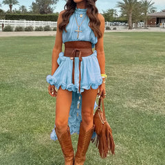Woman in a light blue dress with a brown belt and boots standing on grass.