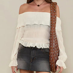 Woman wearing a white off-shoulder top and denim skirt, holding a brown leather bag with eyelets.