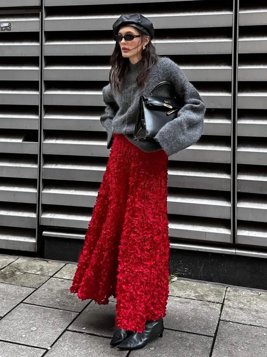 Person wearing a gray sweater, red skirt, and black shoes against a metallic background