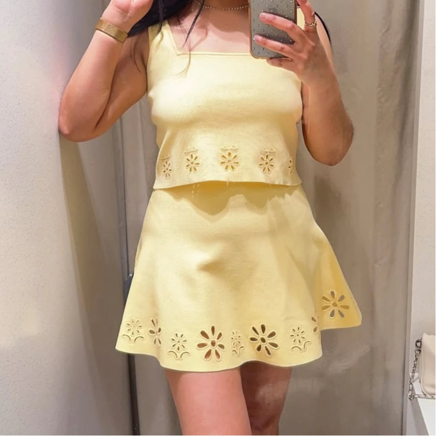 Person wearing a yellow dress with floral cutouts, taking a mirror selfie.