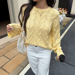 Person wearing a yellow cable knit sweater and white pants, holding a beige handbag and a black coffee cup.