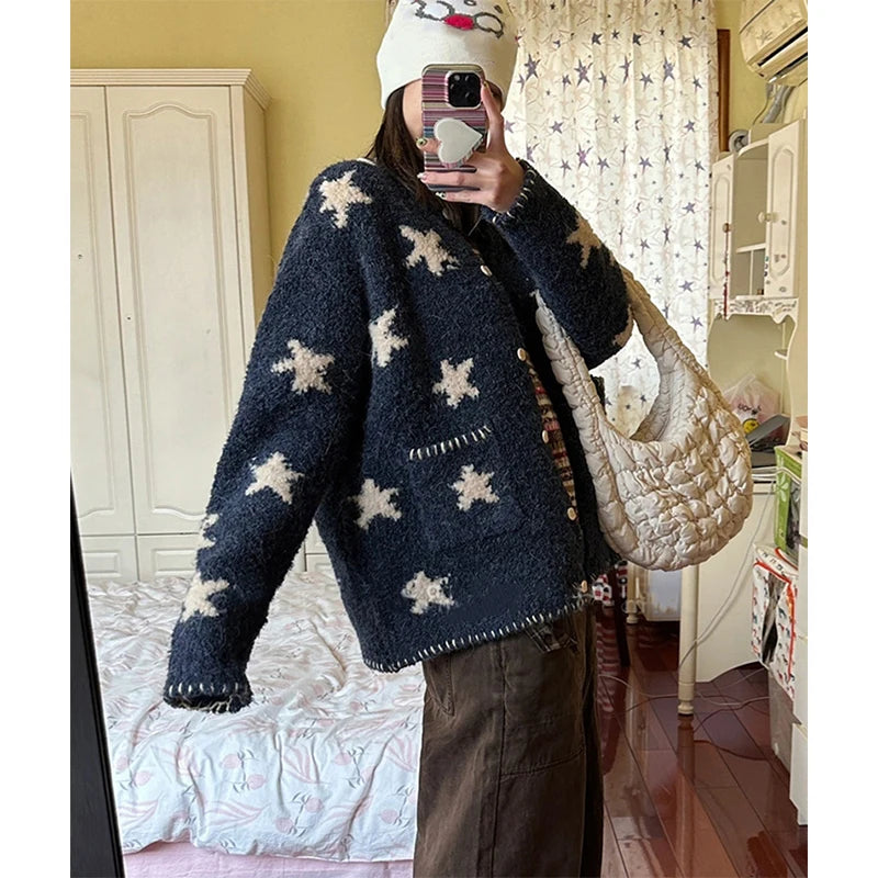 Person wearing a navy blue sweater with white star patterns, holding a beige bag indoors.