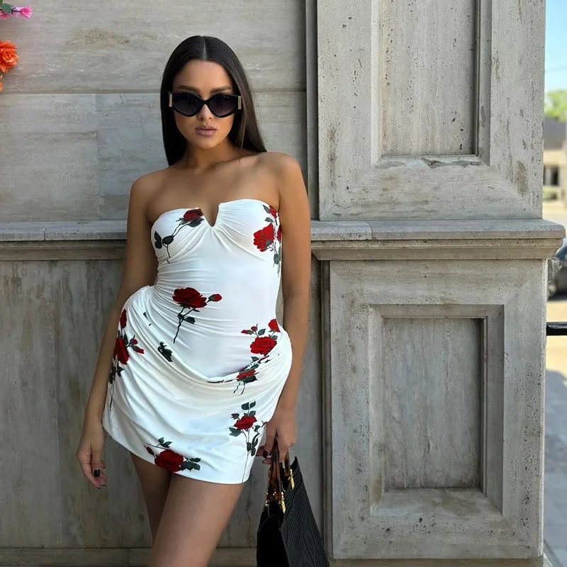 Woman wearing a white strapless dress with red floral patterns against a stone wall.
