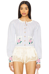 A model wearing a light blue and white vertically striped long-sleeve cardigan with pink rose embroidery on the pockets and cuffs, paired with cream satin bubble shorts, against a plain white background.