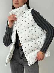 Person wearing a white puffer vest with black floral patterns over a dark outfit on a plain background