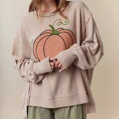 Person wearing a beige sweater with a pumpkin design on a plain background