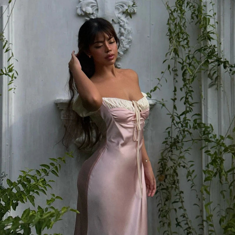Woman in a pink dress standing against a white wall with greenery