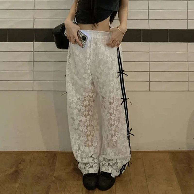 Person wearing floral lace pants with black ribbons against a tiled wall.