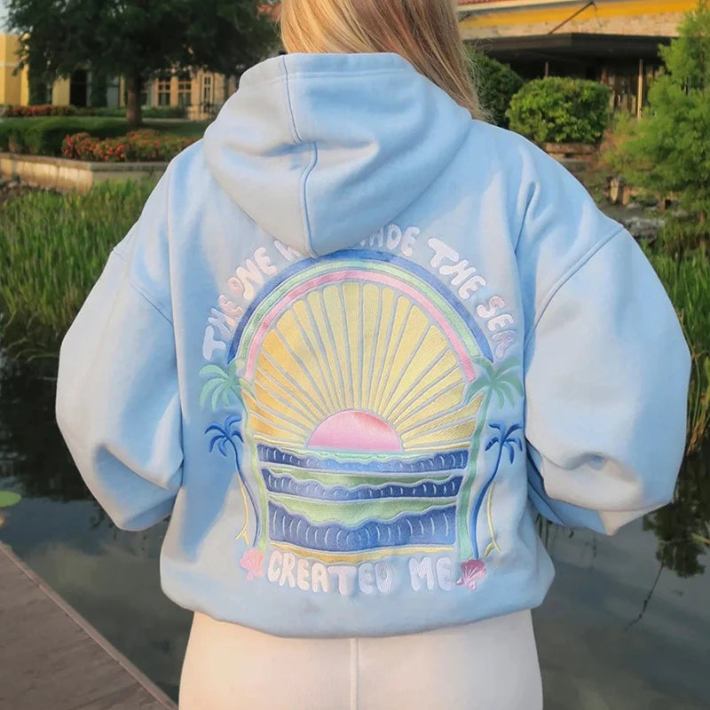 Person wearing a light blue hoodie with a colorful graphic on the back, standing outdoors.