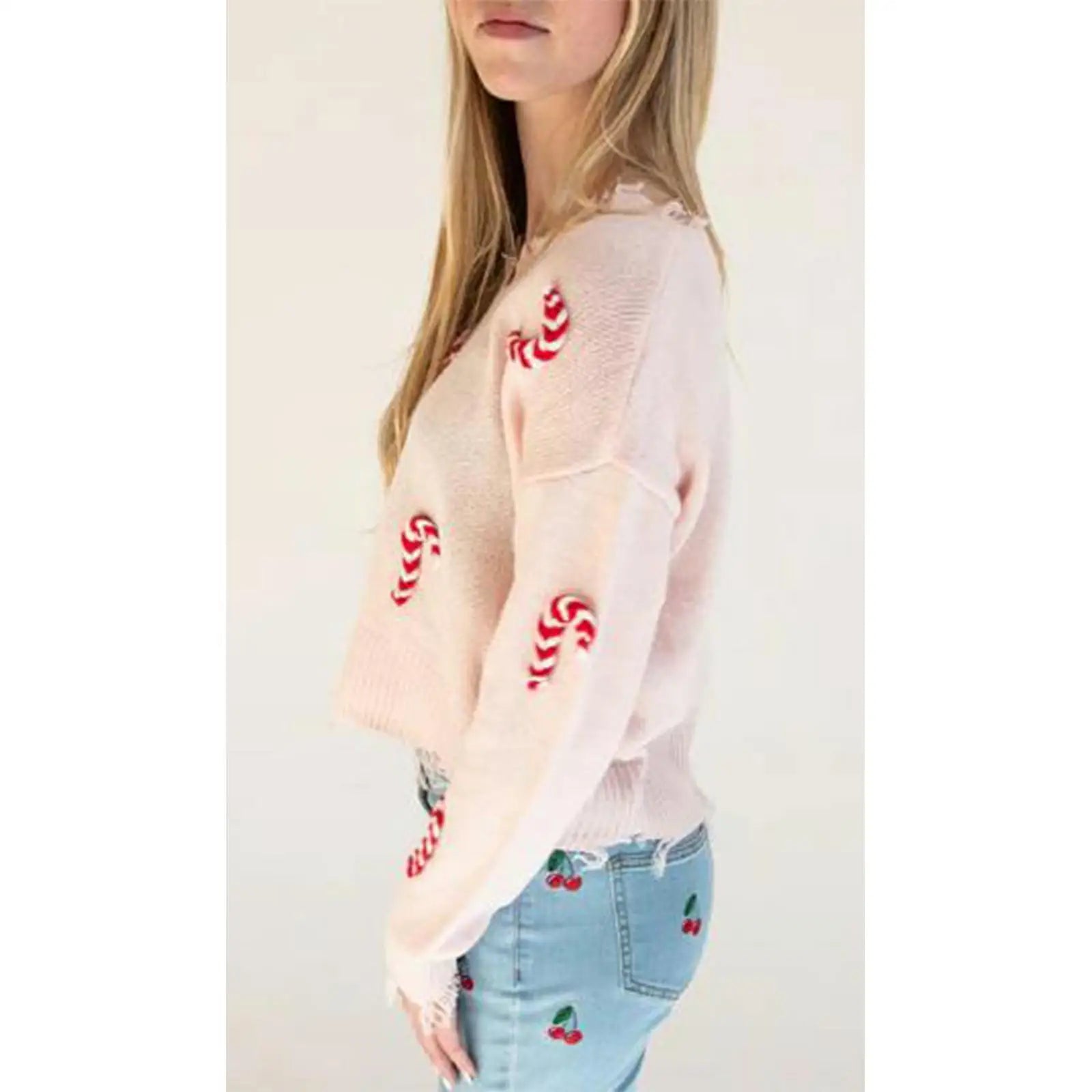 Person wearing a light pink cardigan with red candy cane patterns and blue jeans with cherry patterns.