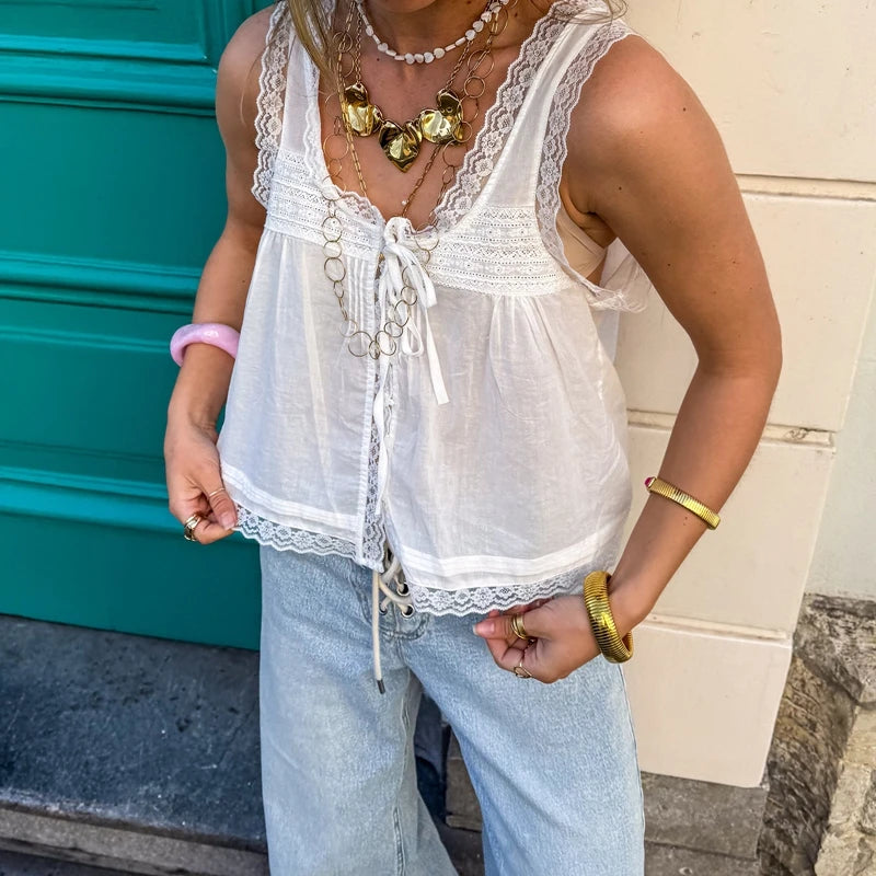 Person wearing a white lace top and light blue jeans with a teal wall in the background