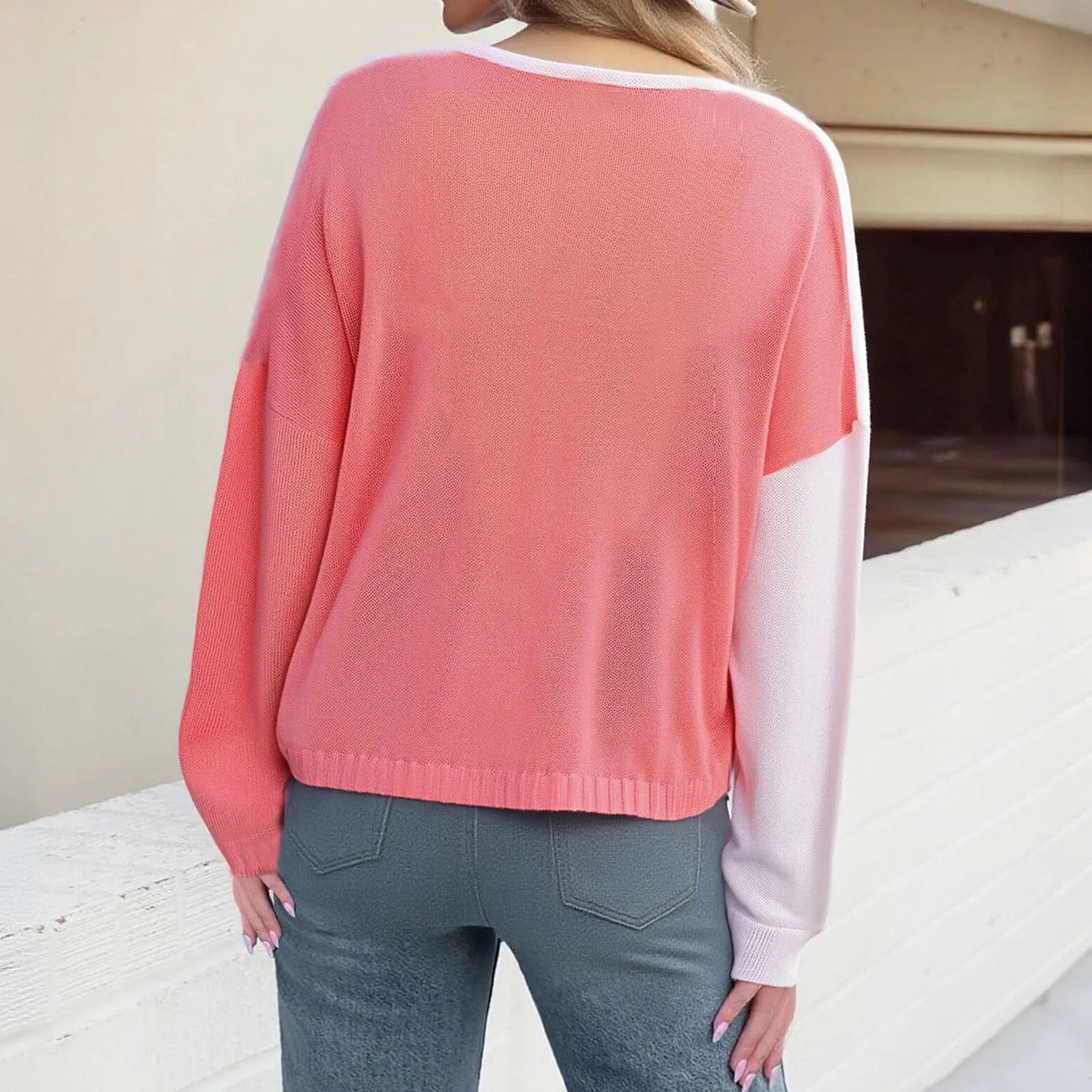 Person wearing a pink sweater with white trim and blue jeans, standing on a wooden deck.