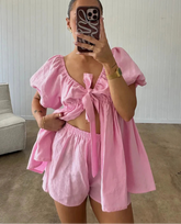 Person wearing a pink outfit with puffed sleeves and a bow detail, standing in a room.