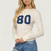 Woman wearing a white long-sleeve shirt with blue number '80' and floral pattern, paired with blue jeans
