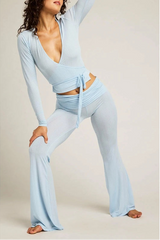 Woman wearing a light blue outfit with long sleeves and wide-leg pants on a plain background