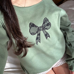 Person wearing a green sweatshirt with a black bow design