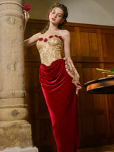 Woman in a gold and red dress holding a rose in an indoor setting.