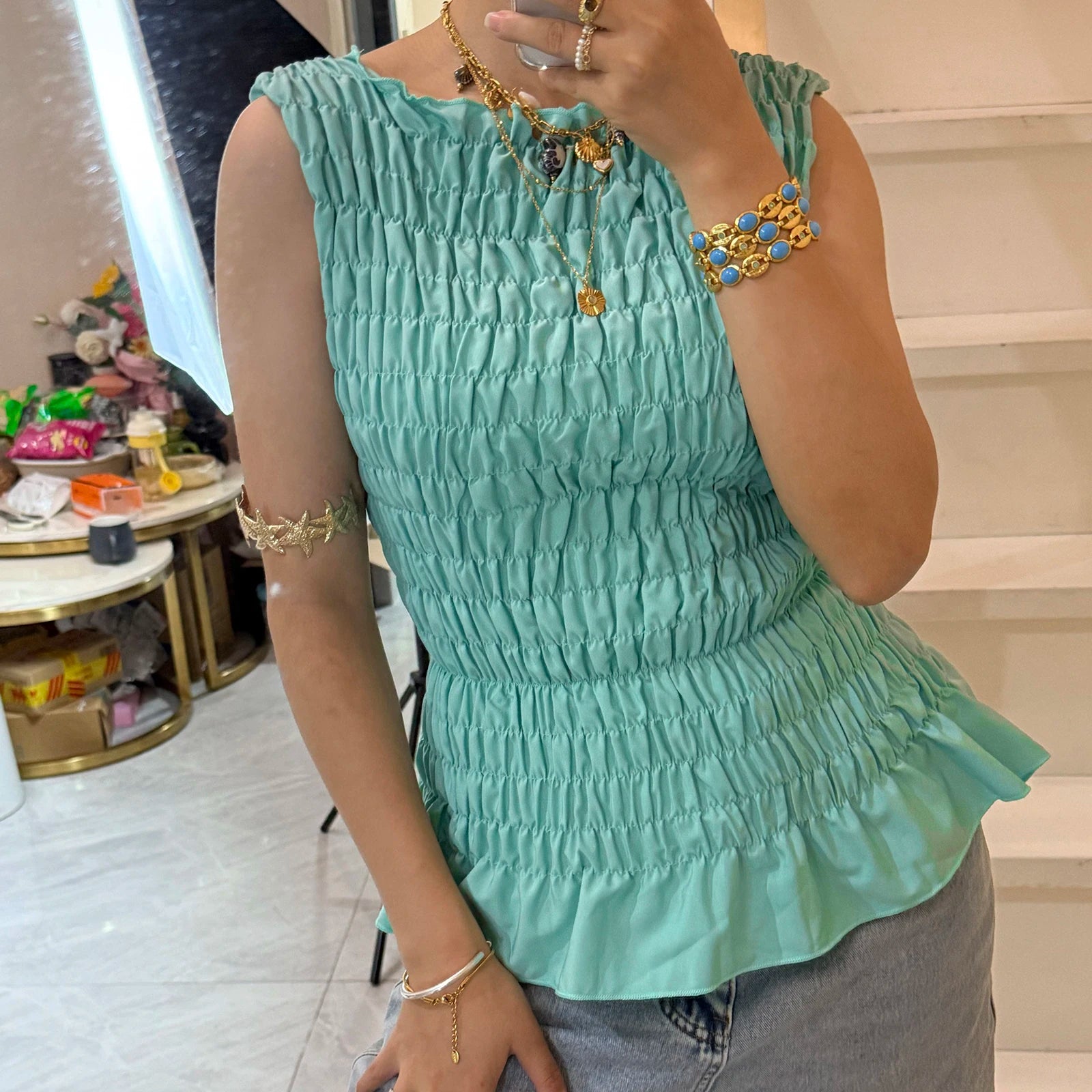 Person wearing a light green sleeveless top with ruffled details, standing indoors.