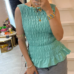 Person wearing a light green sleeveless top with ruffled details, standing indoors.