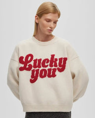 Person wearing a cream sweater with 'Lucky you' text in red on a plain background