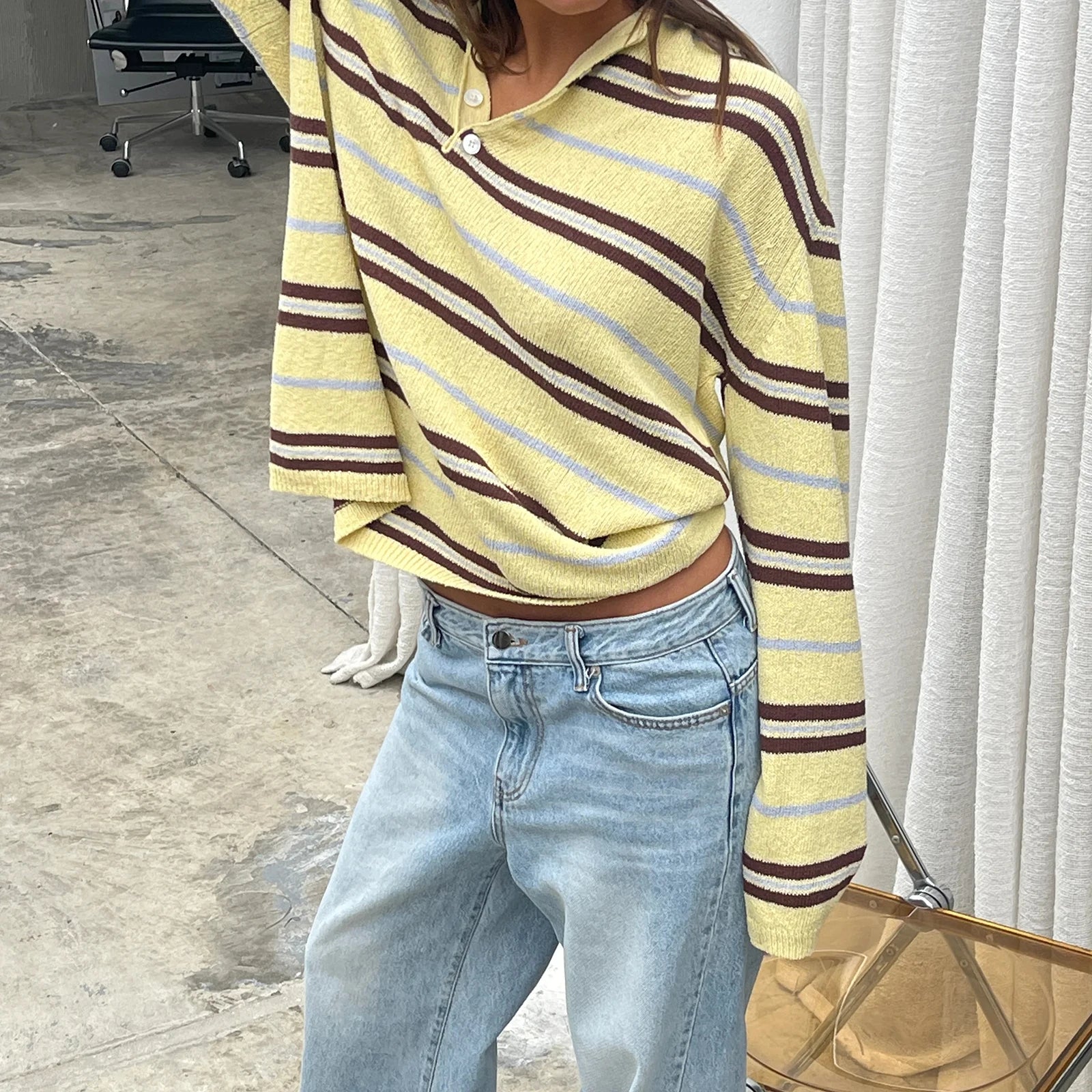Person wearing a yellow and brown striped sweater with light blue jeans indoors.
