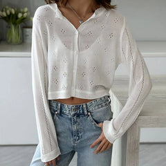 Person wearing a white embroidered cardigan and blue jeans indoors.