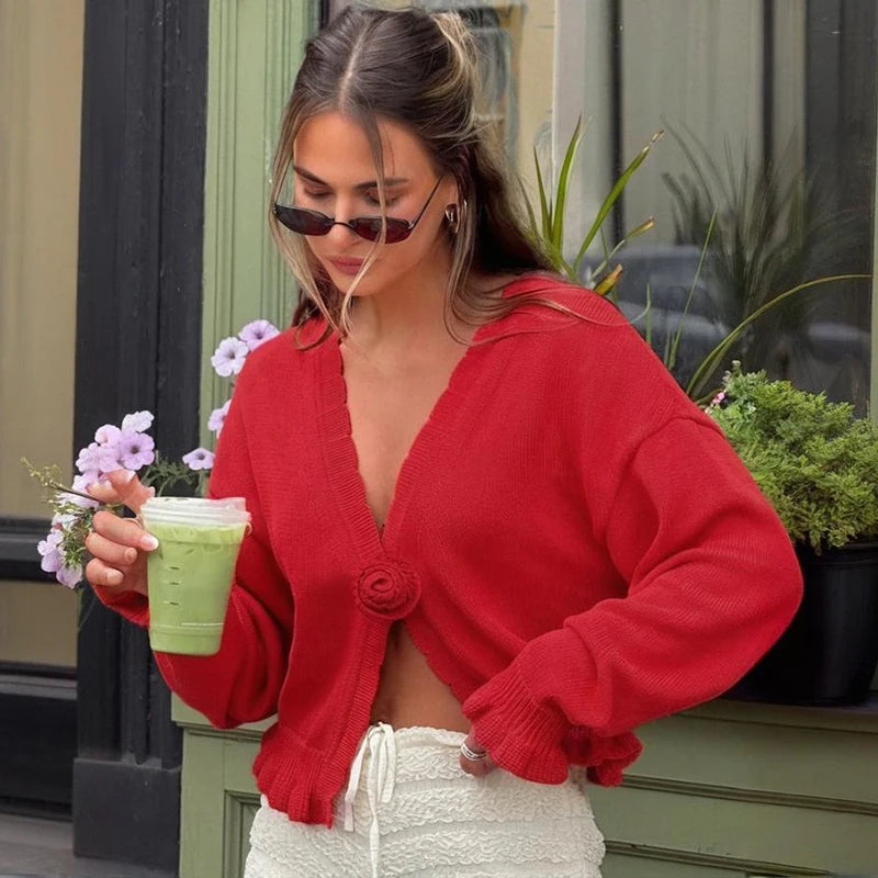 Woman in a red cardigan holding a green smoothie with plants in the background