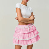 Person wearing a white top and pink checkered skirt with lace trim on a plain background