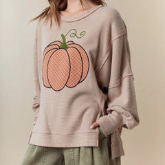 Person wearing a beige sweatshirt with a pumpkin graphic on a beige background