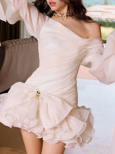 Woman wearing a one-shoulder beige dress with ruffled details.