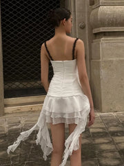 Woman wearing a white dress with black straps in an urban setting.