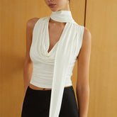 Woman wearing a white sleeveless top with a draped design against a mustard yellow background